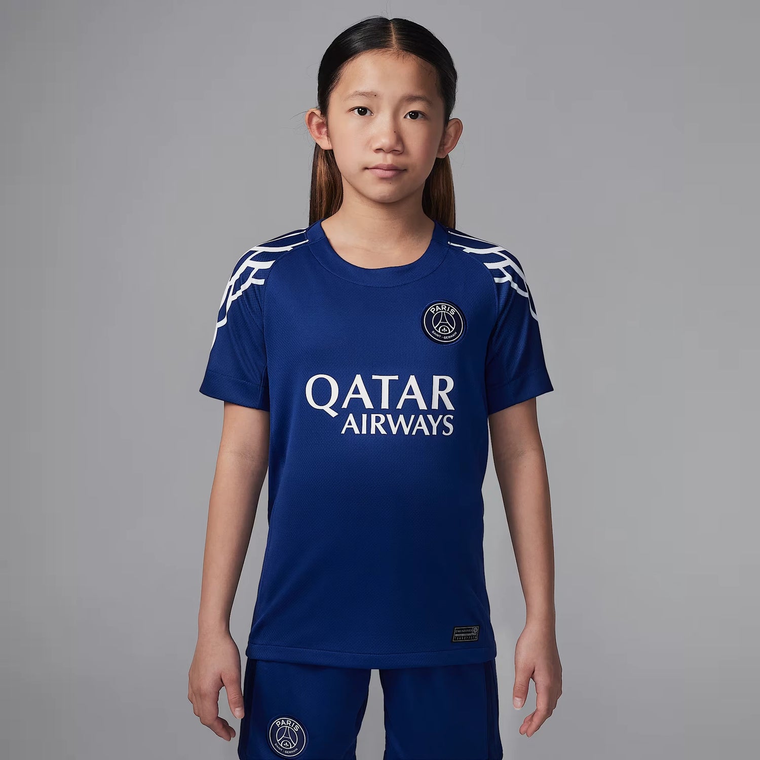 Ett barn bär Paris Saint-Germains fjärdetröja för säsongen 2024/25 i marinblått, med Qatar Airways som sponsor och Jordan-logotyp på bröstet.