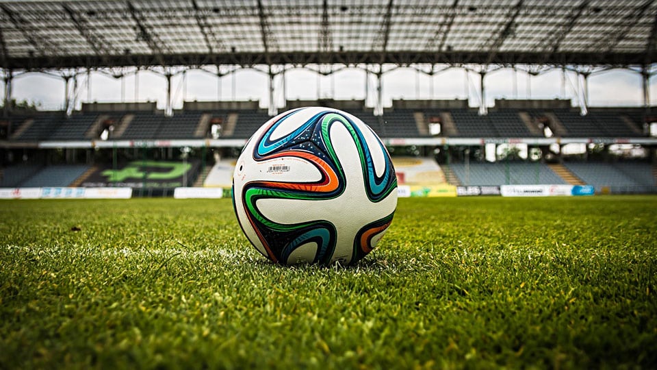 Färgglad fotboll på en tom gräsplan i ett stadion – symboliserar passionen bakom Proffsdräkten.se fotbollströjor från toppklubbar.